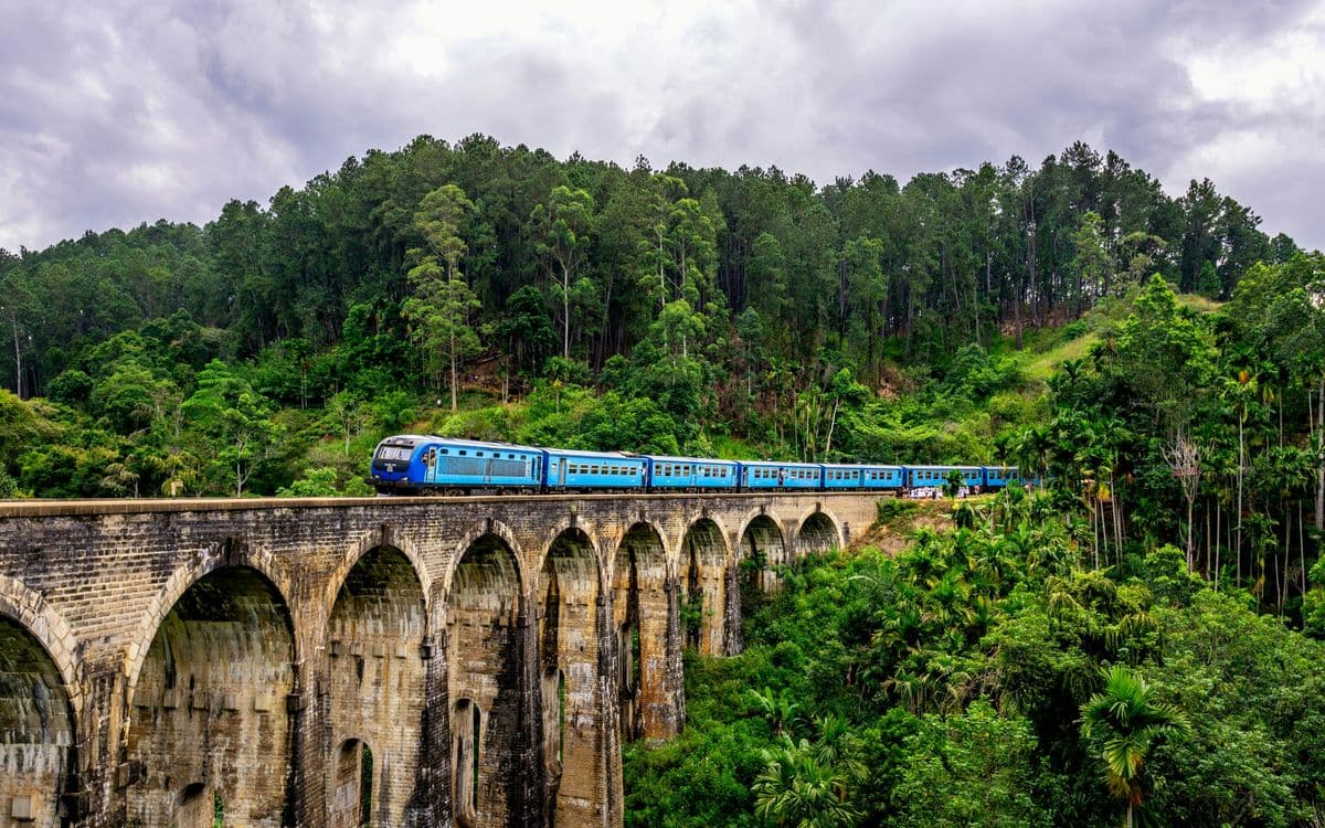 Blue train crossing the Nine Arch Bridge in Ella surrounded by lush green jungle