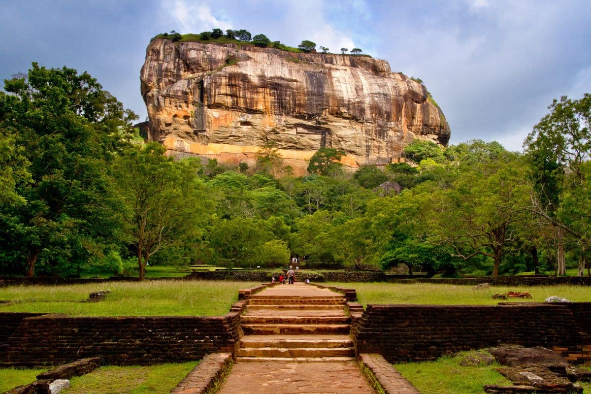 Sigiriya Lion Rock fortress rising above lush green gardens, ancient steps leading to the rock, Sri Lanka